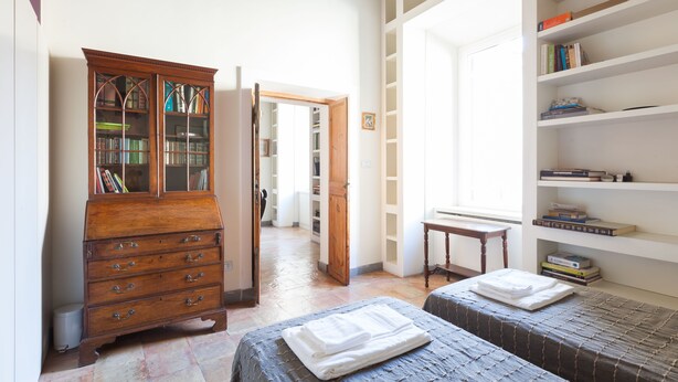 A room with two beds, a wooden dresser, and a bookshelf. - Habitat's Campo di Fiori Apartments (Rome)