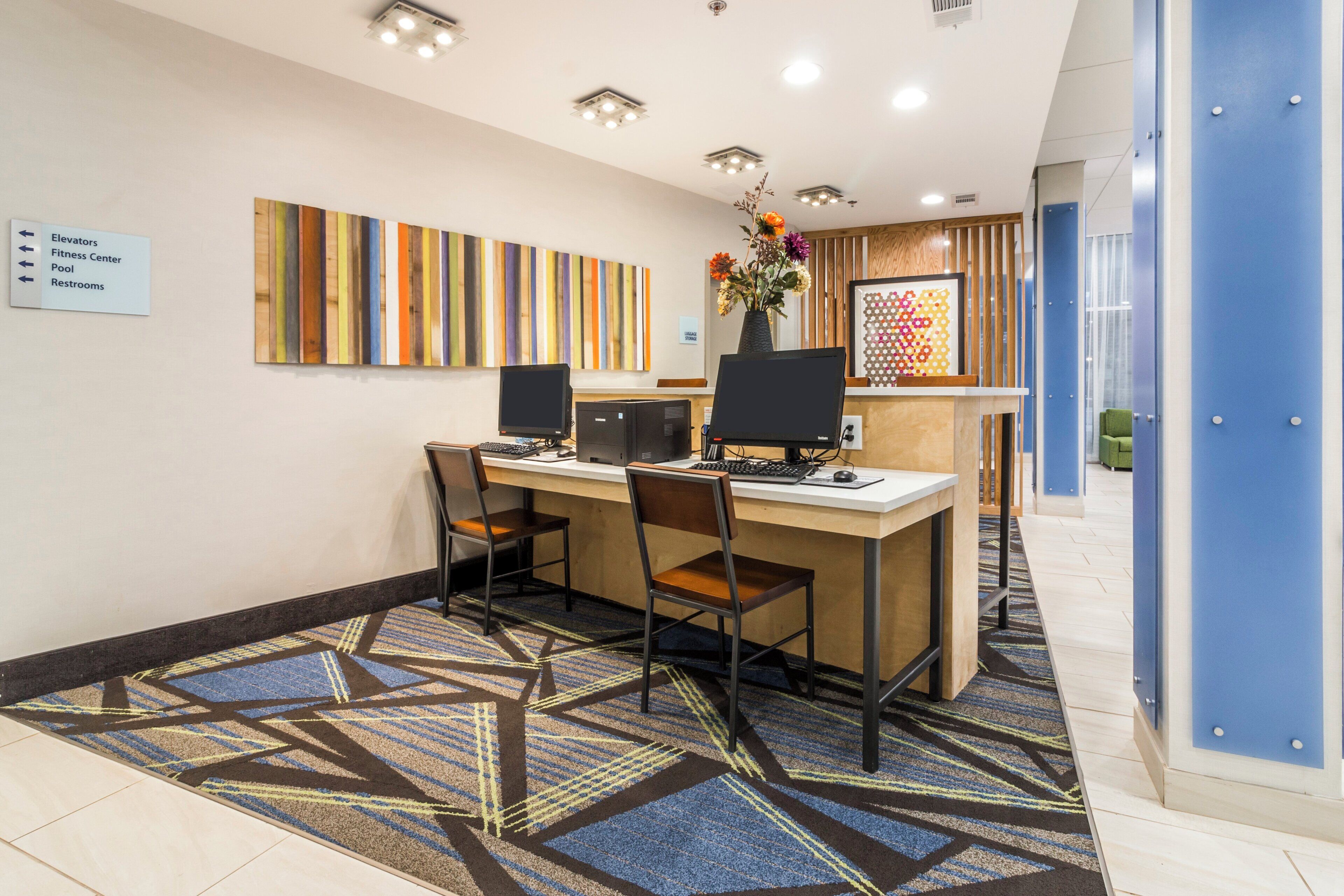 A reception area with a desk, two chairs, a computer, and a vase with flowers.