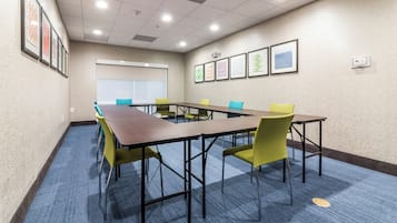 A conference room with a long table, chairs, a projector screen, and framed artwork on the walls.