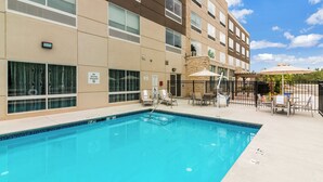A swimming pool with a pool lift, lounge chairs, and umbrellas, surrounded by a building with multiple windows and a clear sky. - Holiday Inn Express Villa Rica by IHG (Villa Rica)