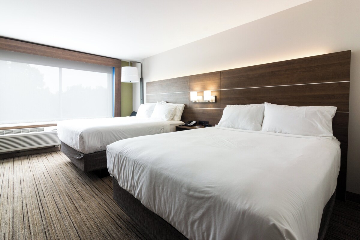 Habitació d'hotel amb dos llits, una finestra gran, una làmpada penjada a la paret i un calefactor integrat.