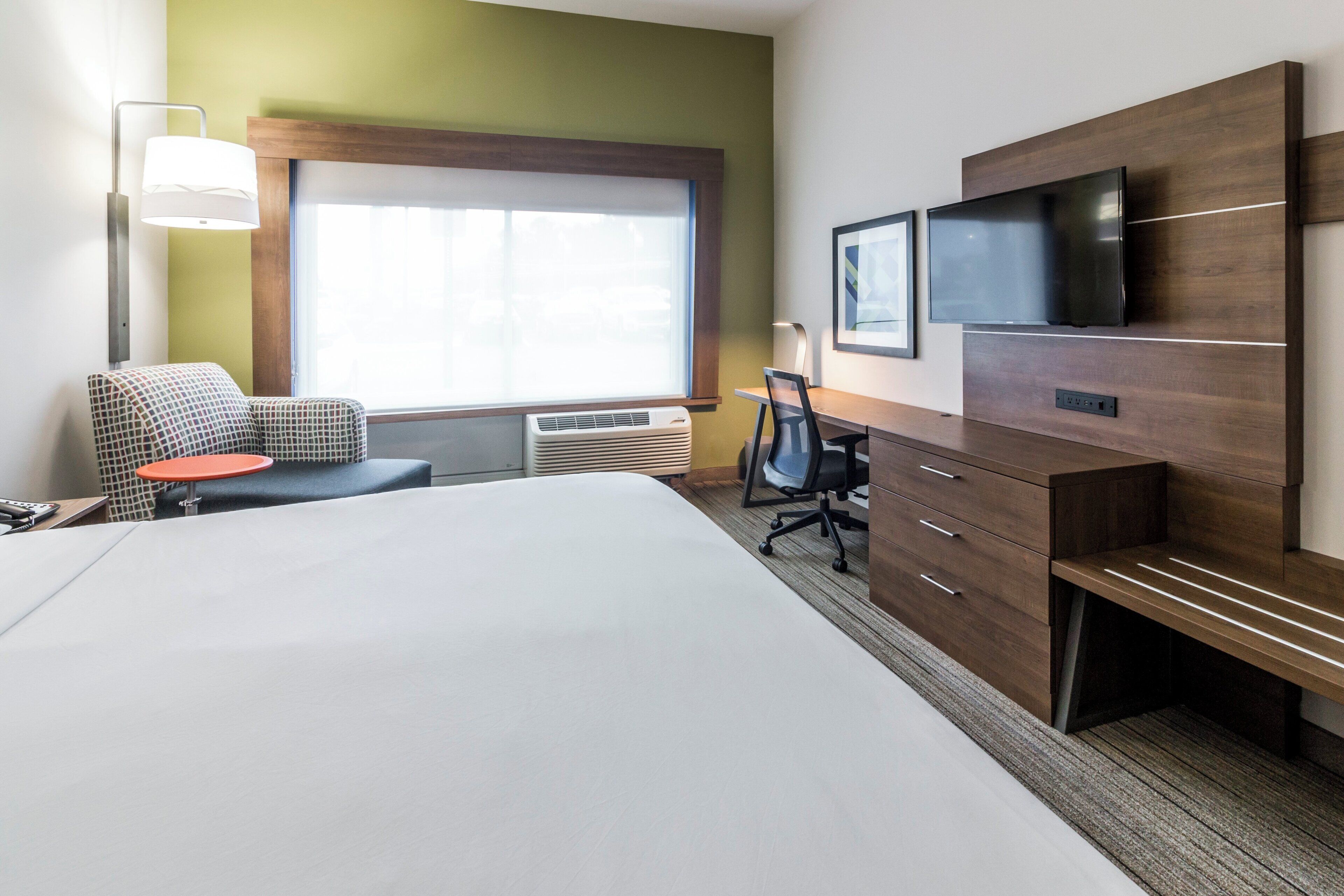 A hotel room with a large bed, a desk, a chair, a TV, and a window with blinds.