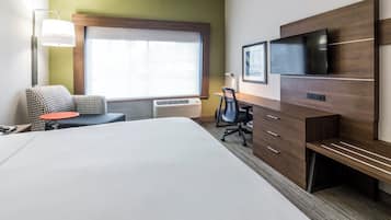 A hotel room with a large bed, a desk, a chair, a TV, and a window with blinds.