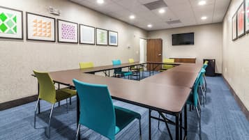 Ein Konferenzraum mit einem langen Tisch, blaugrünen Stühlen und gerahmten Kunstwerken an den Wänden.