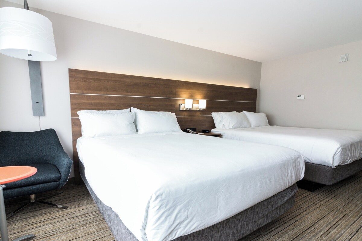 Una habitació d'hotel amb dos llits, un escriptori, una cadira i una làmpada.