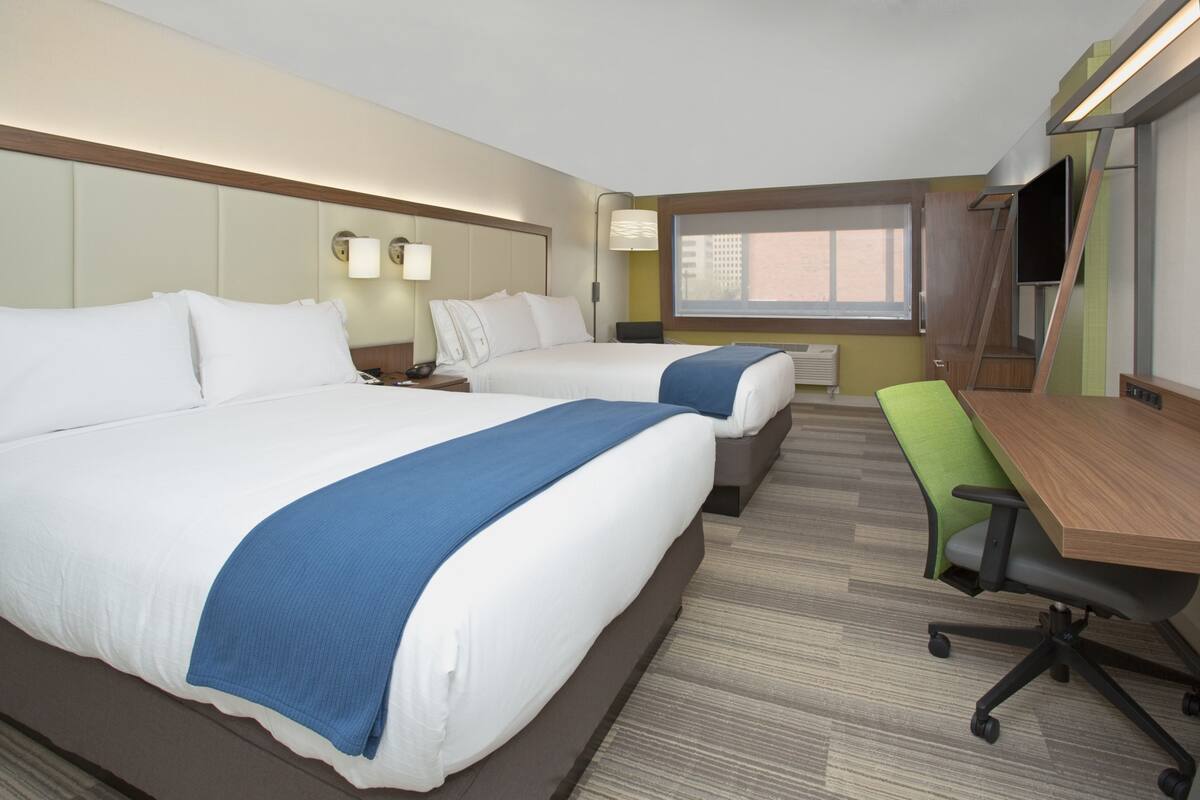 A hotel room with two beds, a desk, a chair, and a large window.