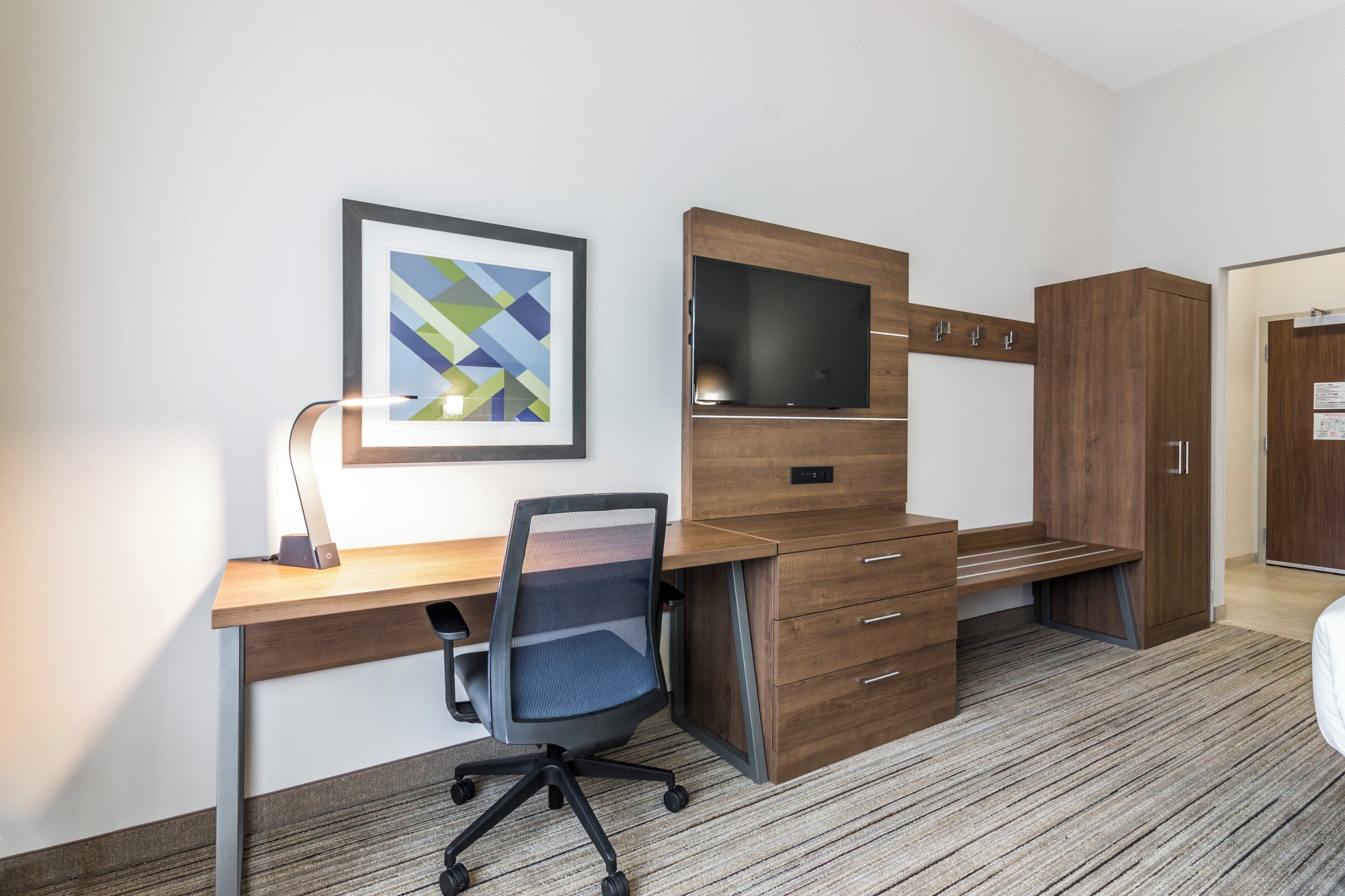 A modern office space with a desk, chair, TV, and wooden cabinets.