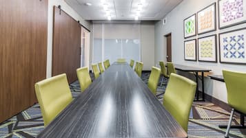 A conference room with a long table, yellow chairs, and framed artwork on the walls.