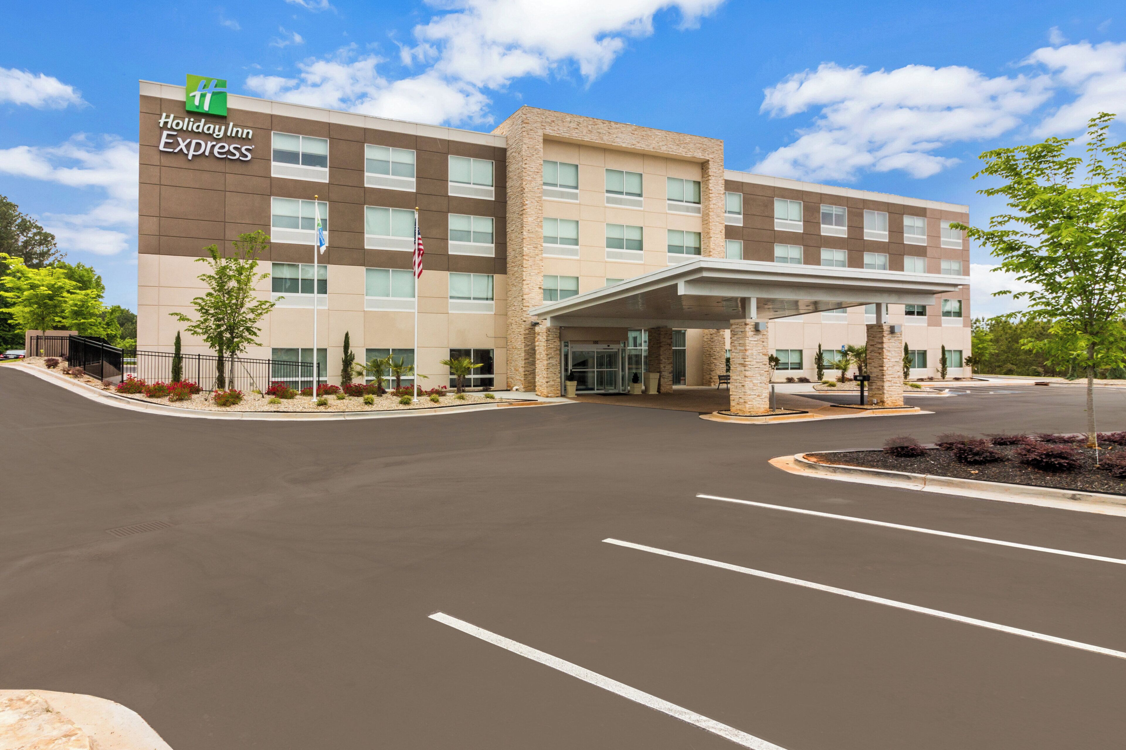 A Holiday Inn Express building with a covered entrance, a parking lot, and a landscaped area with trees.