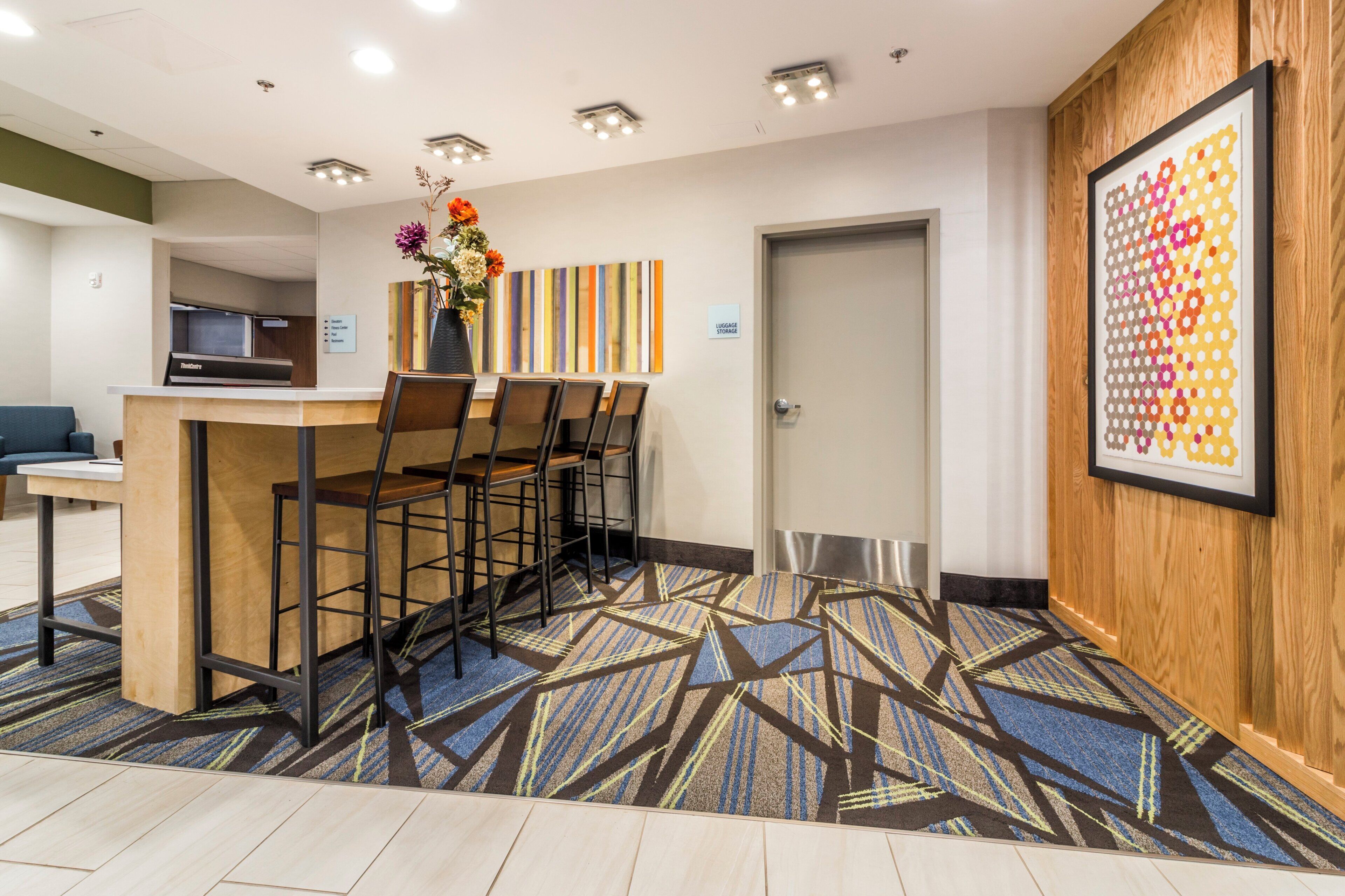 A hotel reception area with a reception desk, chairs, a vase with flowers, a wall-mounted artwork, and a luggage storage sign.