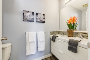 A modern bathroom with a toilet, two white towels, a sink with a mirror, and two floral paintings on the wall. - Superb 3BR mins to DT SAIT (Calgary)