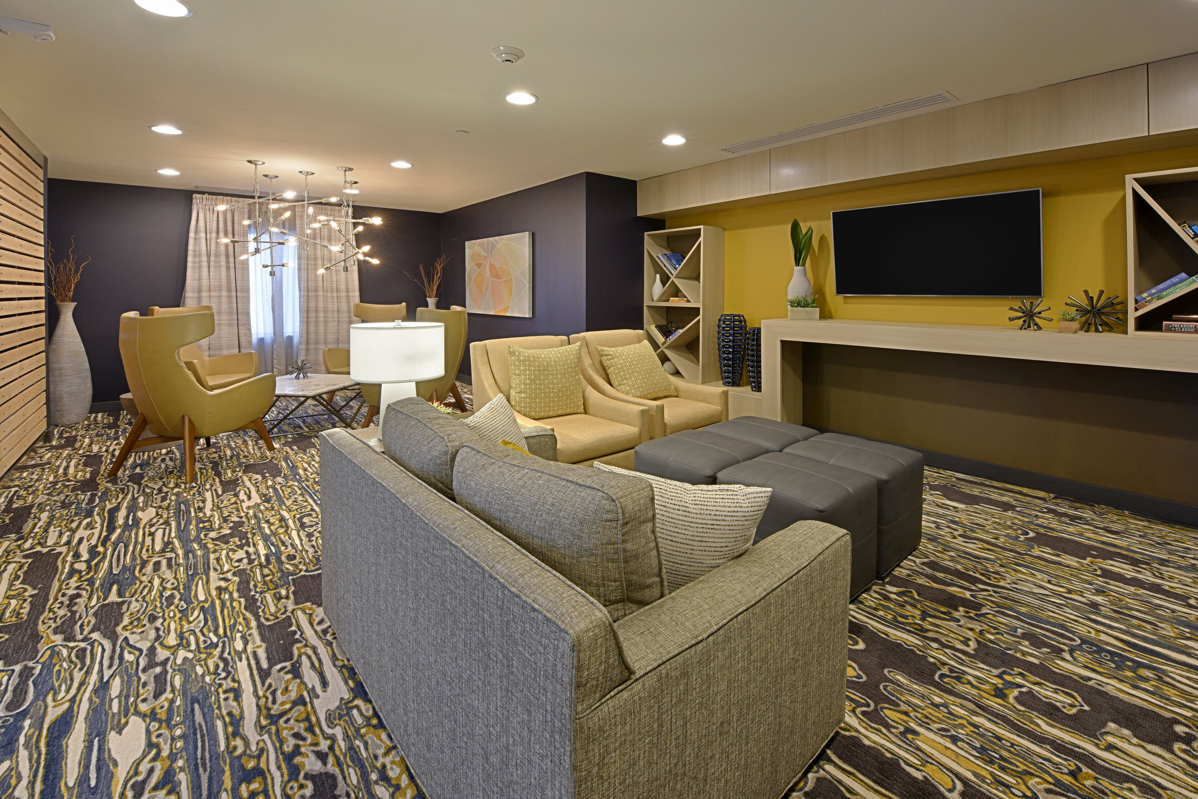 Una habitación de hotel moderna con sofá, sillones, televisor de pantalla plana y un elemento decorativo en la pared.