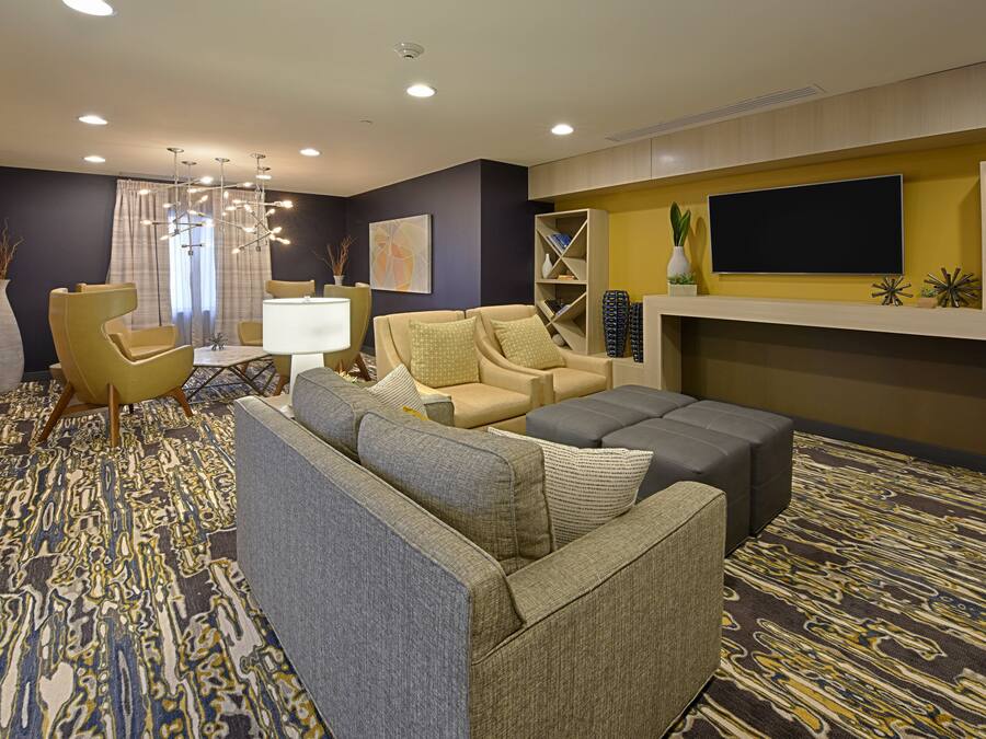 Una habitación de hotel moderna con sofá, sillones, televisor de pantalla plana y un elemento decorativo en la pared.