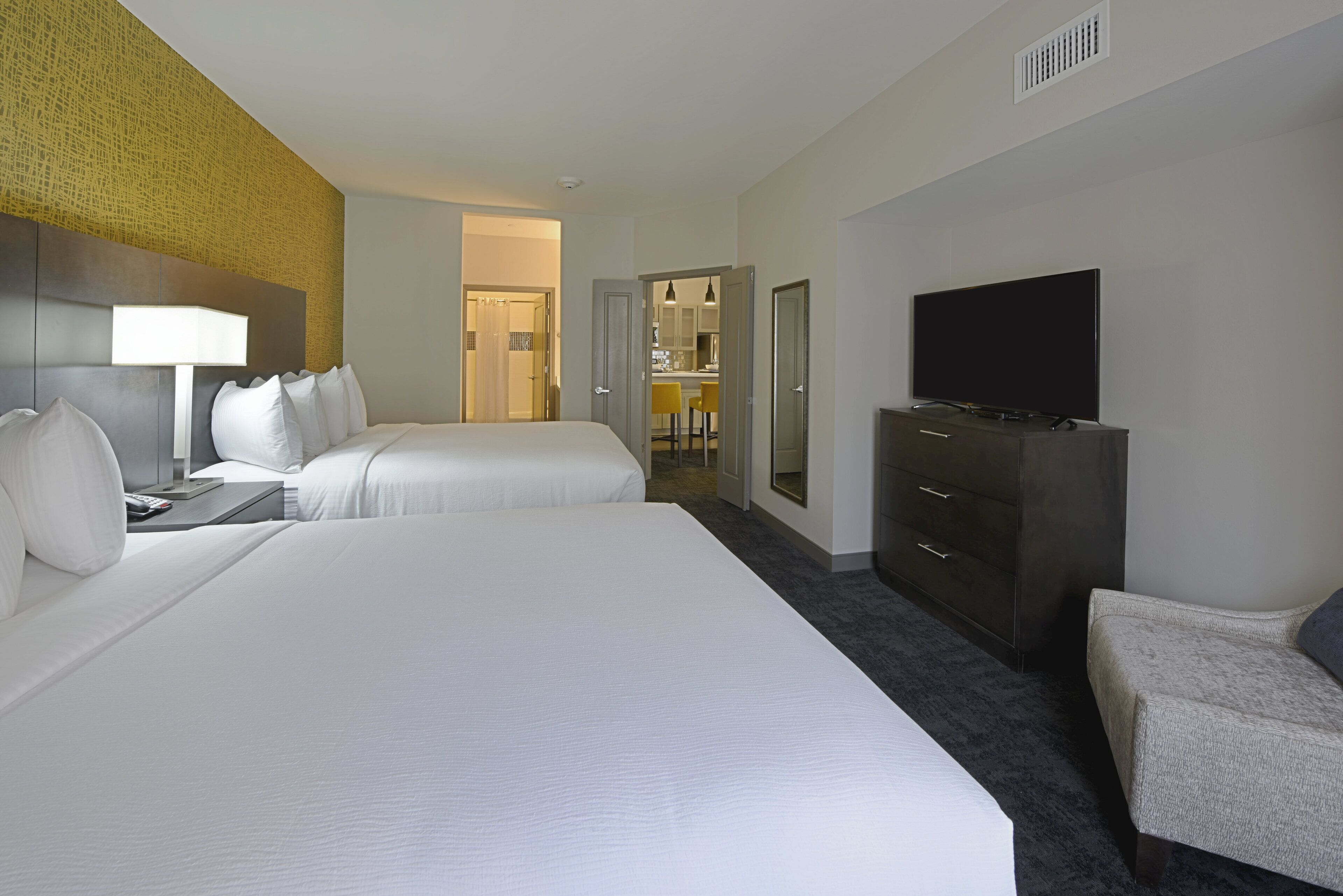 Une chambre d’hôtel avec deux lits, une télévision, un bureau et une salle de bain visible à travers une porte ouverte.