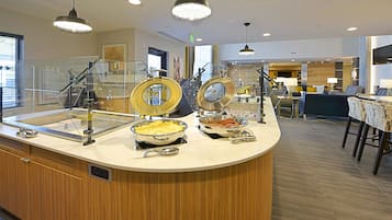 Uma área de buffet com diversos pontos de comida, um extintor de incêndio e uma barreira de vidro transparente.
