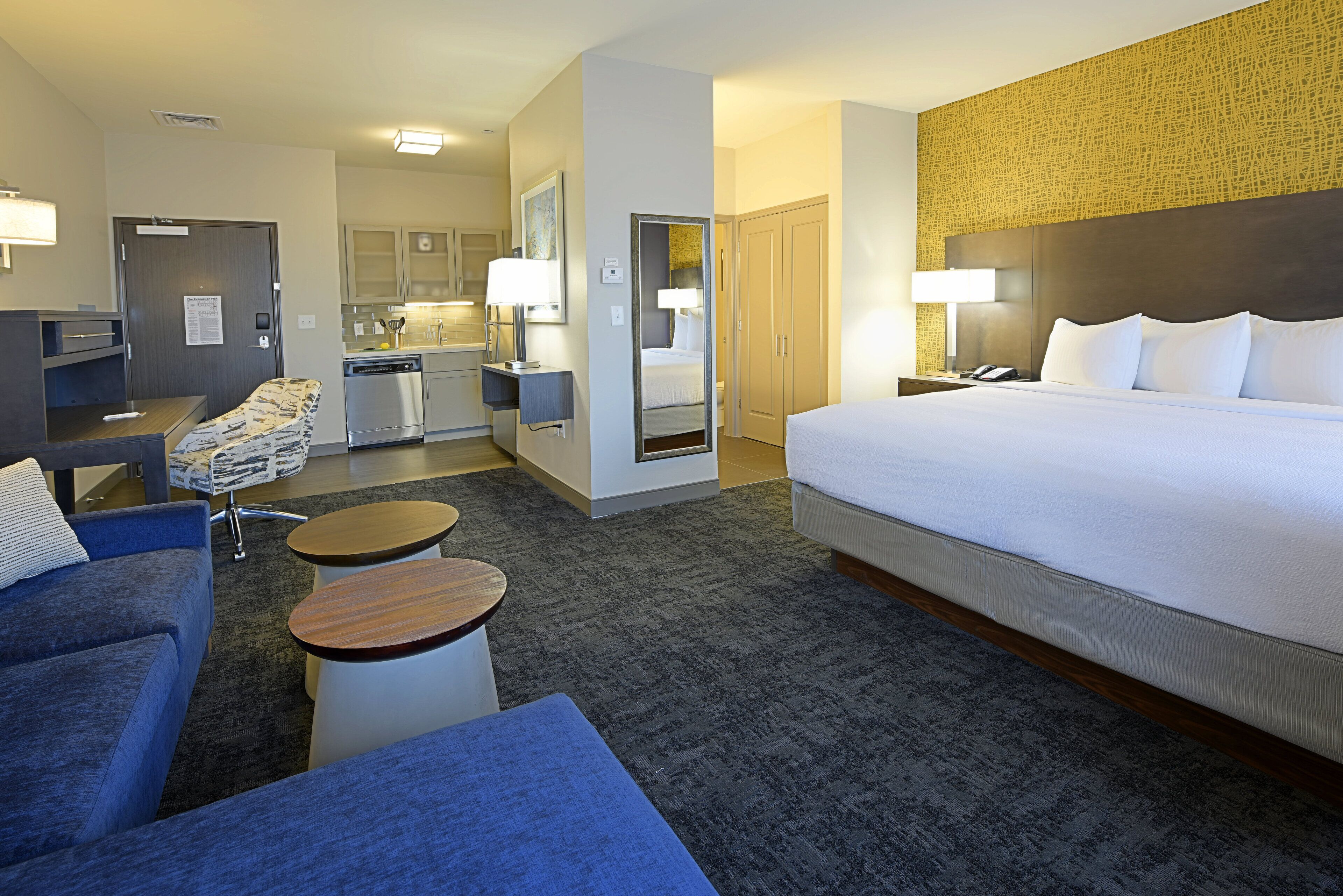 Una habitación de hotel con cama, escritorio, silla, mesita y sofá.
