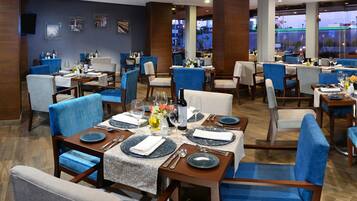 Un restaurante con varias mesas dispuestas para comer, con sillas tapizadas en azul y mesas de madera.