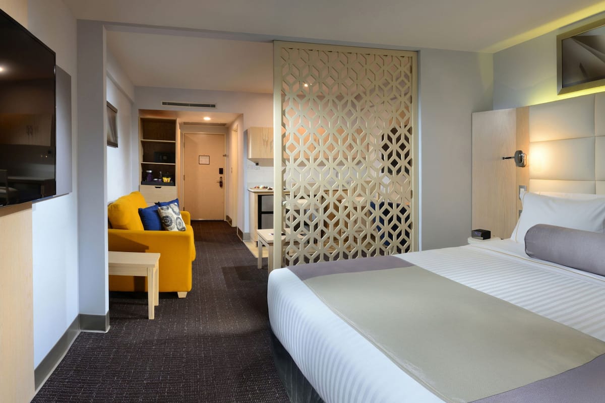 A hotel room with a bed, a sofa, a TV, and a partition wall.