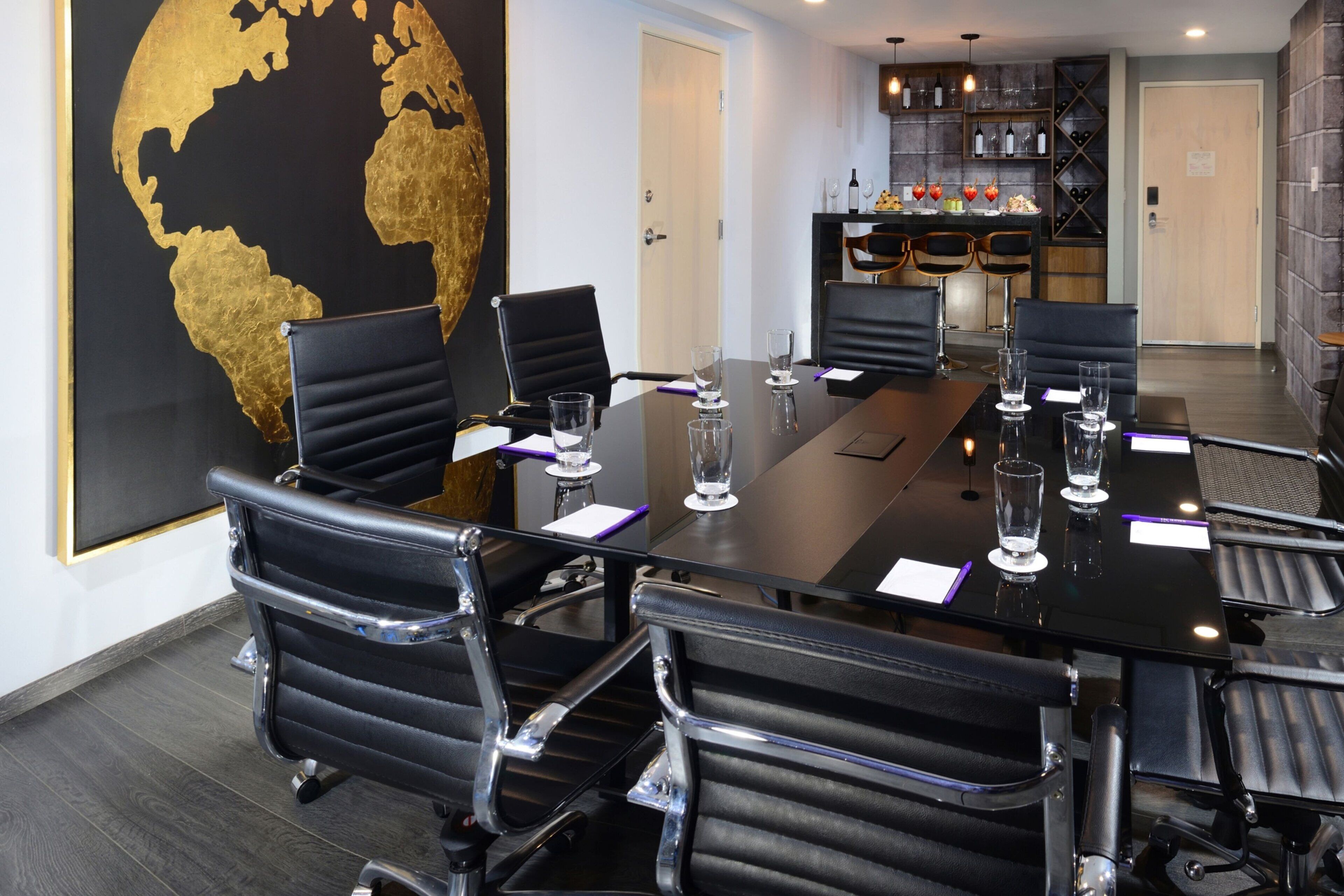 Uma sala de conferência com uma mesa comprida, seis cadeiras de couro preto e um grande mapa-múndi na parede.