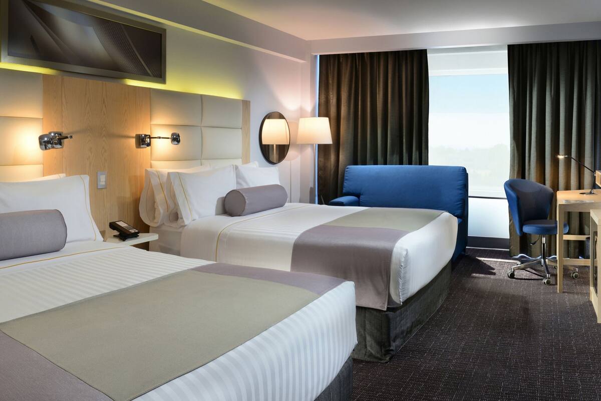 A hotel room with two beds, a desk, a chair, a TV, and a window with curtains.