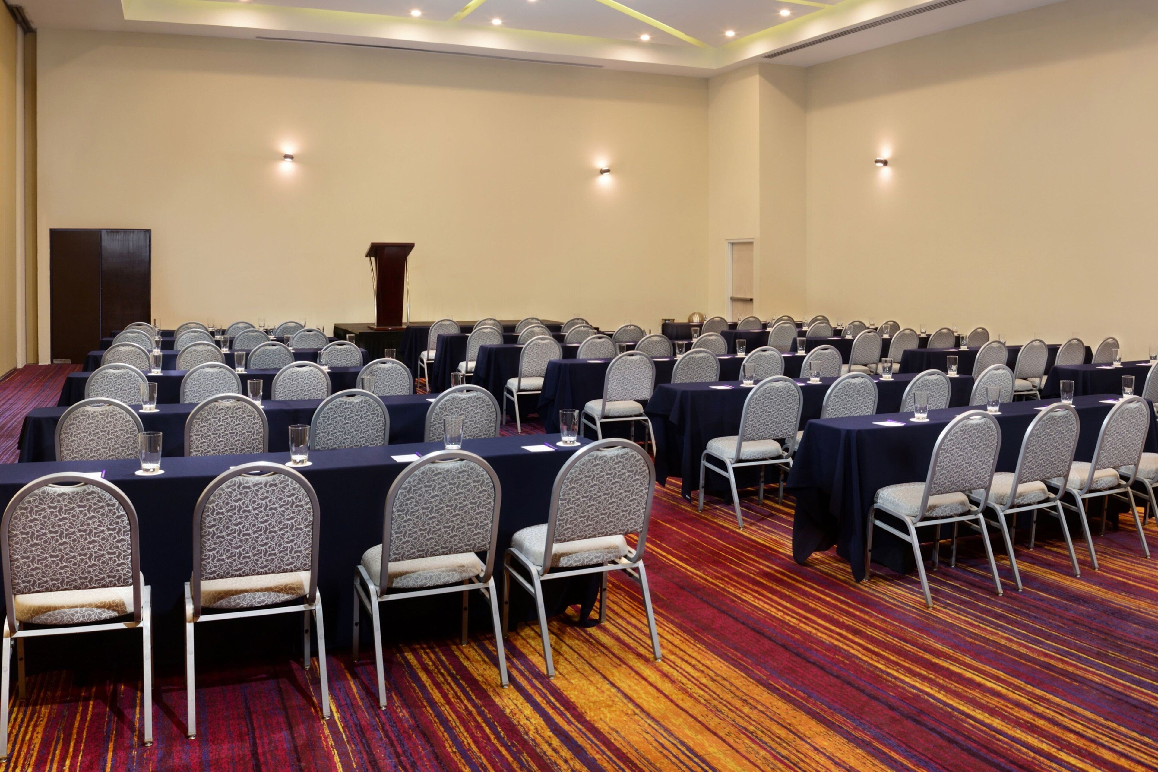 A conference room with multiple tables and chairs, a podium, and a carpeted floor.