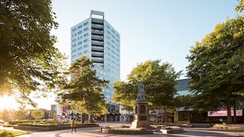 Stroll through the serene public square, surrounded by lush flower beds and trees, with the iconic Crowe Plaza building in the background.