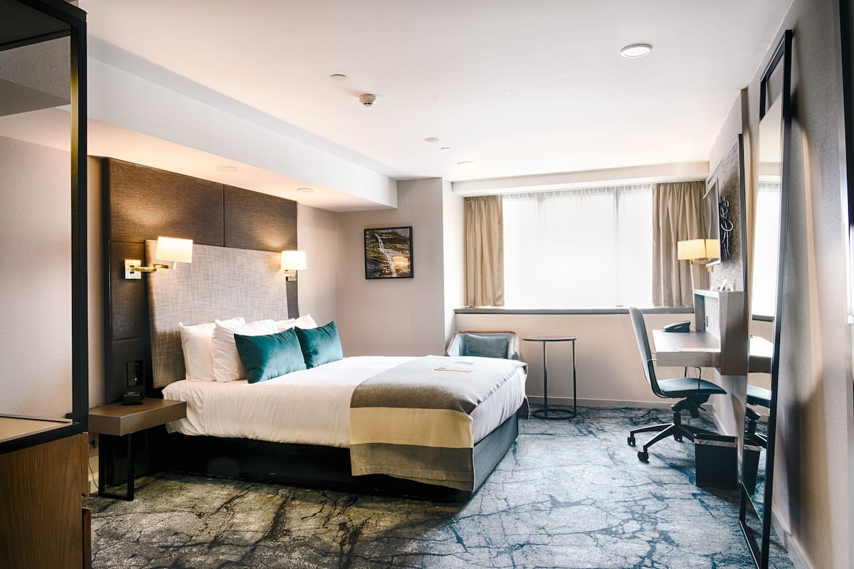 A hotel room with a bed, desk, chair, and a view of the outdoors.