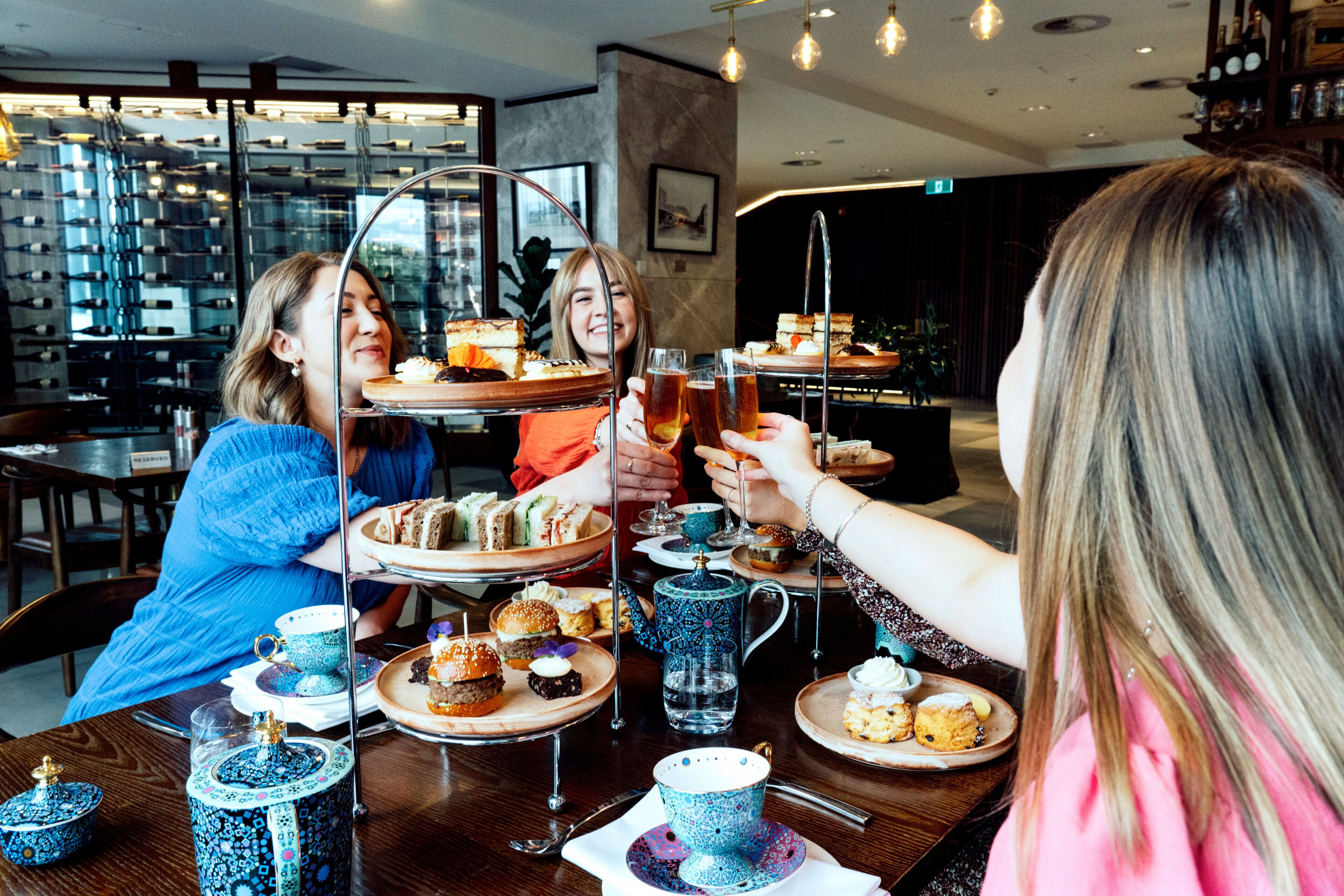 Un grupo de personas brindando con bebidas en una mesa con juegos de té y un pastelero de varios niveles.