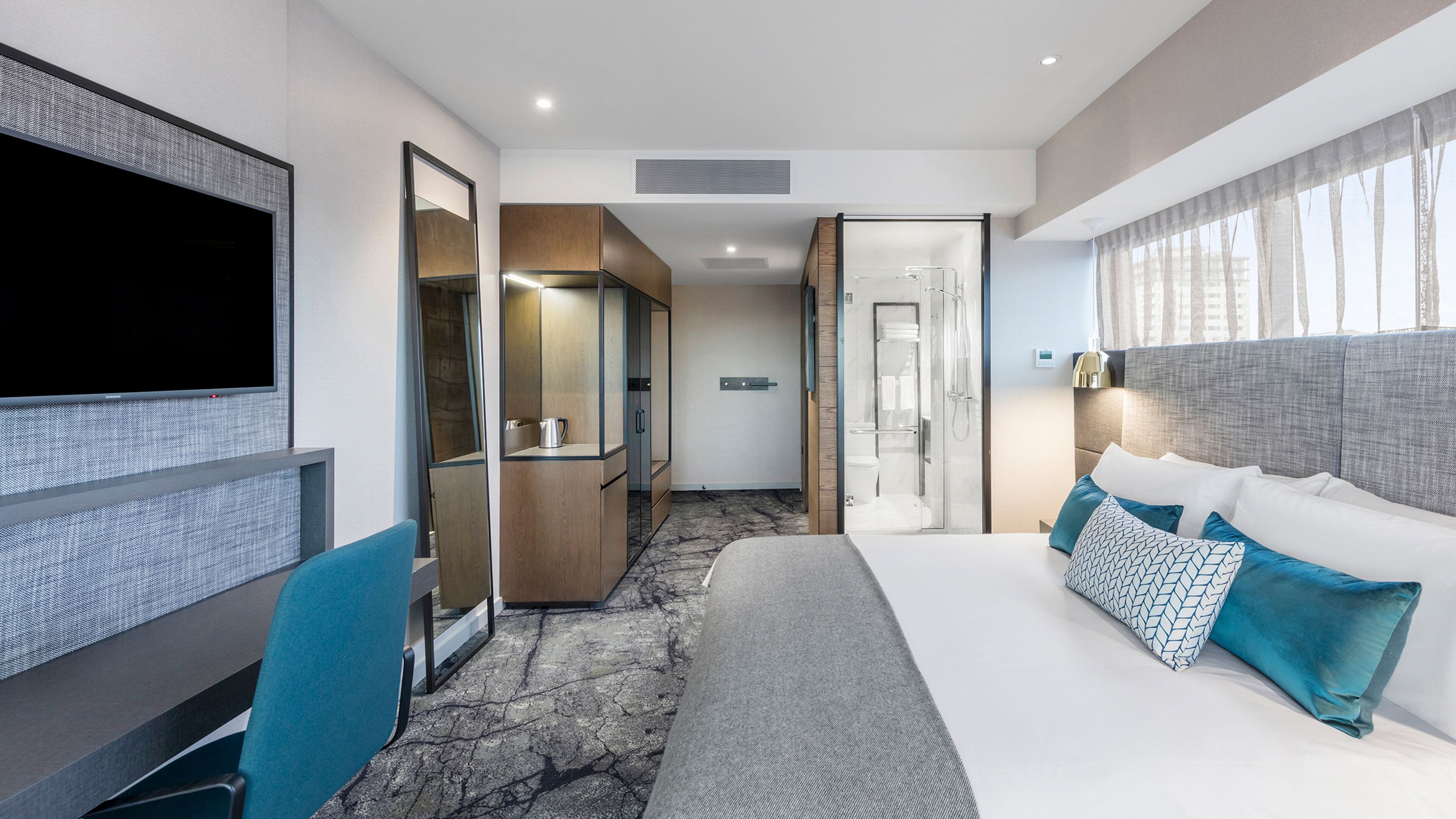 Una habitación de hotel moderna con una cama grande, un escritorio, un televisor y un baño con ducha e inodoro.