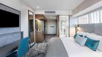 Una habitación de hotel moderna con una cama grande, un escritorio, un televisor y un baño con ducha e inodoro.