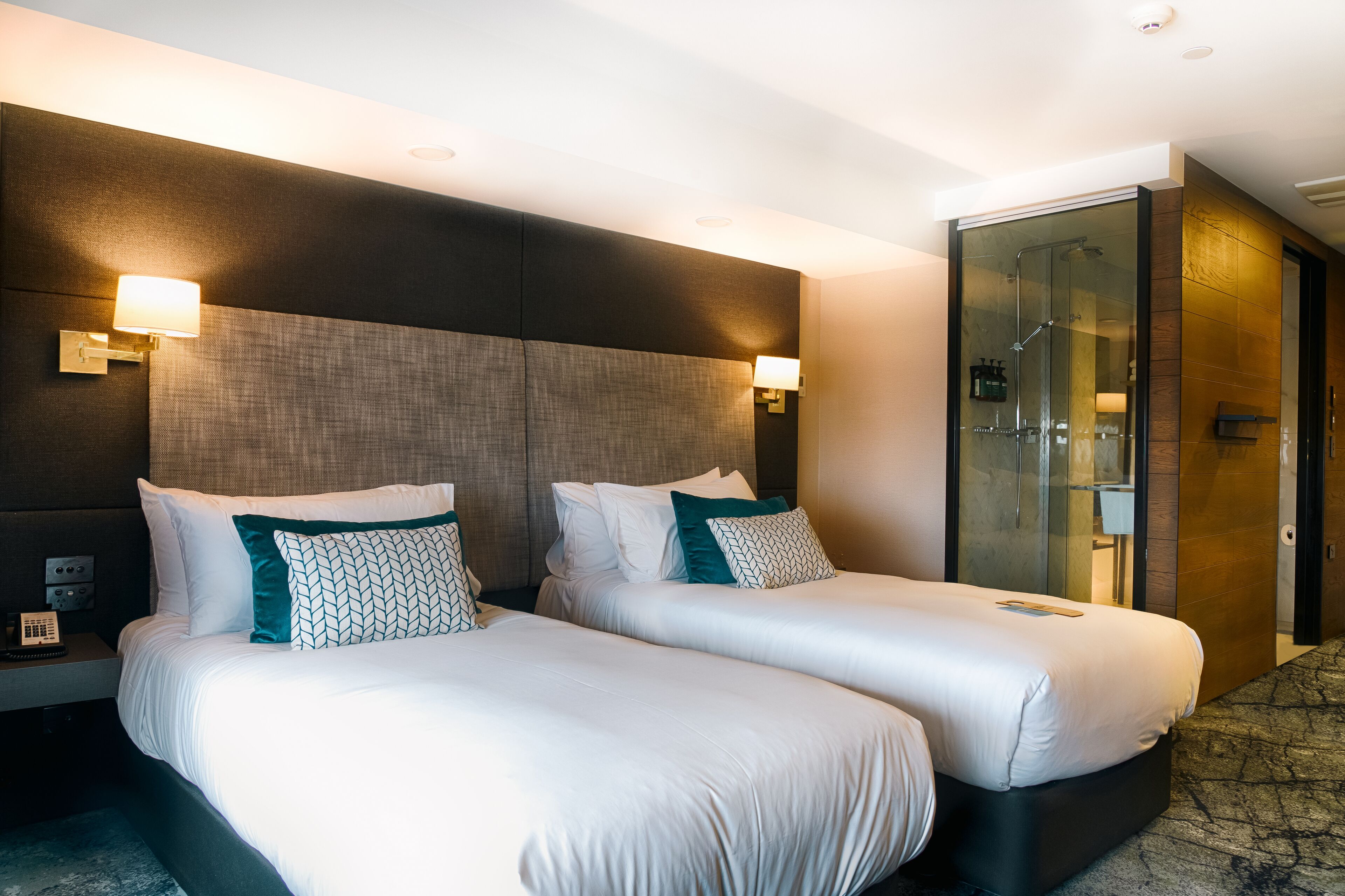 A hotel room with two beds, a glass shower enclosure, and a bedside telephone.
