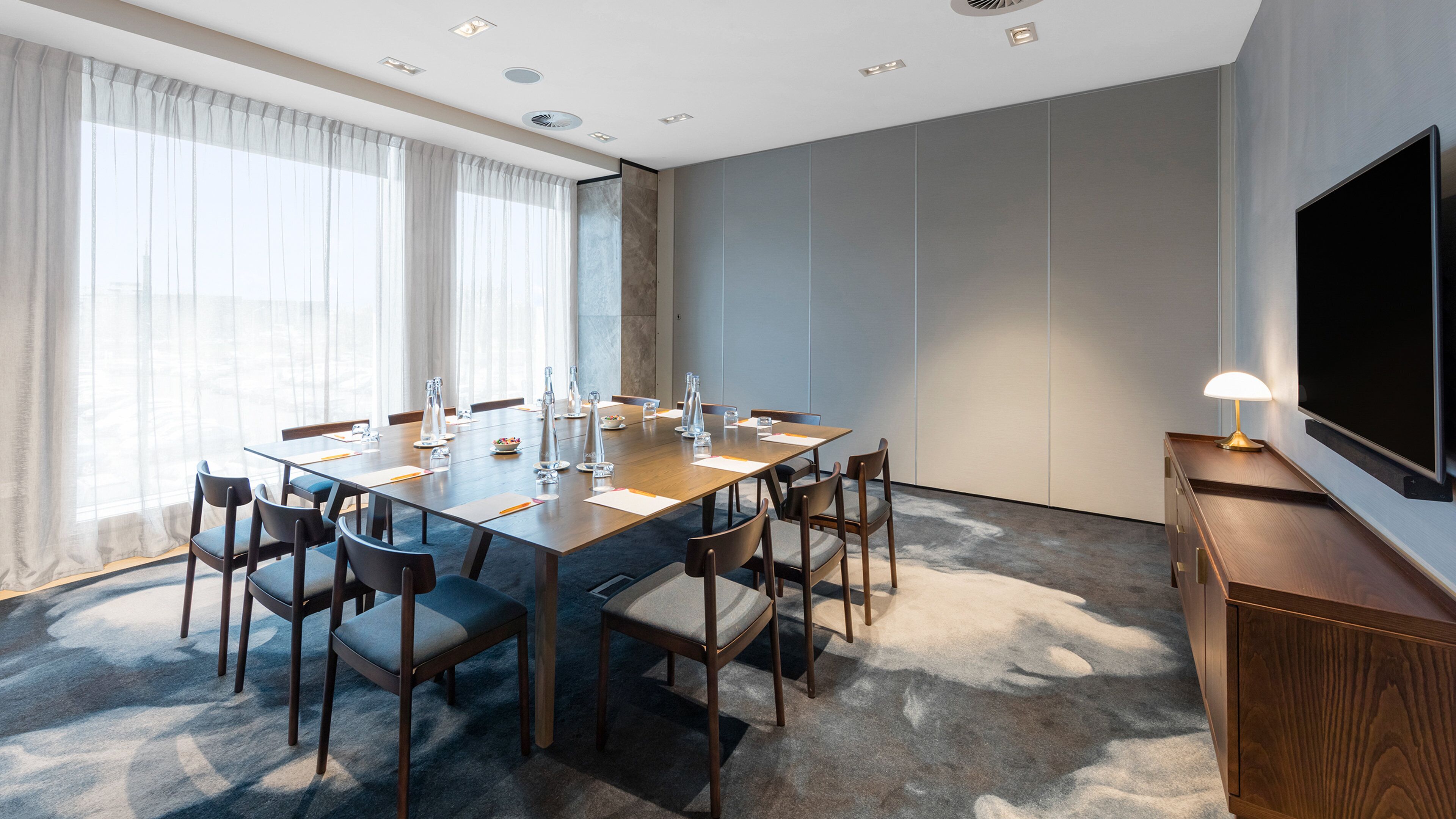 A conference room with a long table, chairs, a TV, and a lamp.