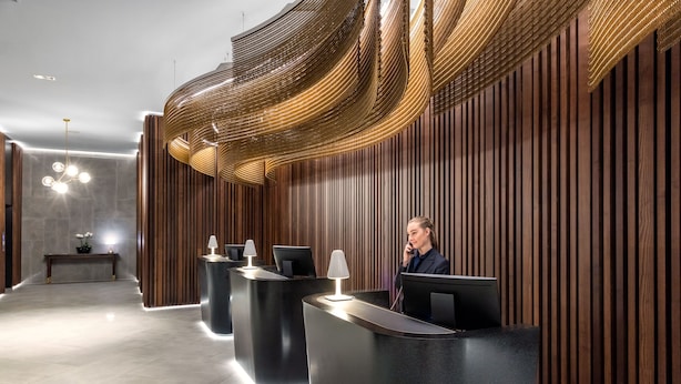 A modern reception area with a receptionist, wooden paneling, and a unique ceiling design.