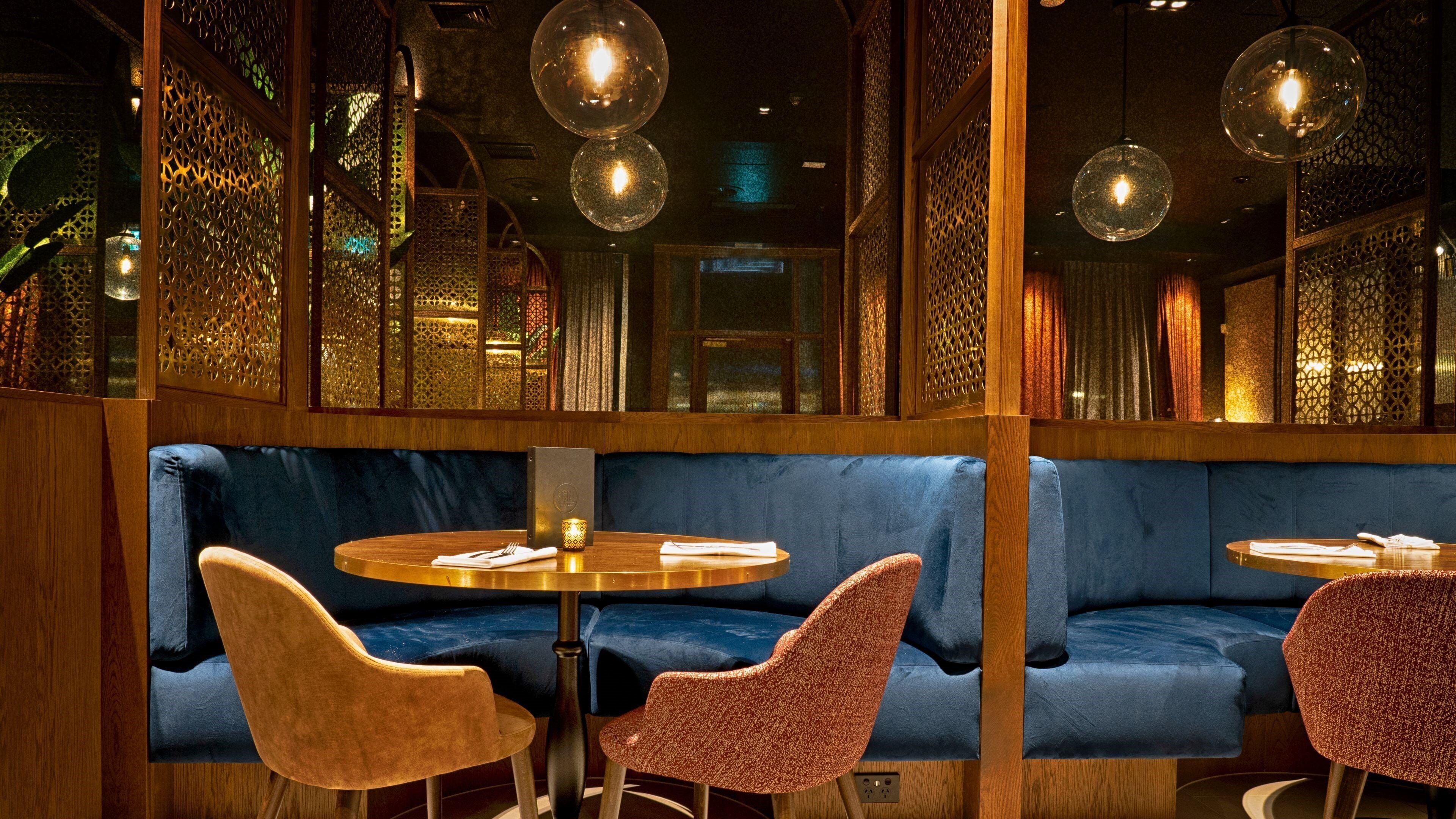 Interior de restaurante con mesas redondas, asientos acolchados en tono azul y lámparas esféricas colgantes.