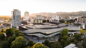 A modern building with a unique architectural design, surrounded by other urban structures and greenery.