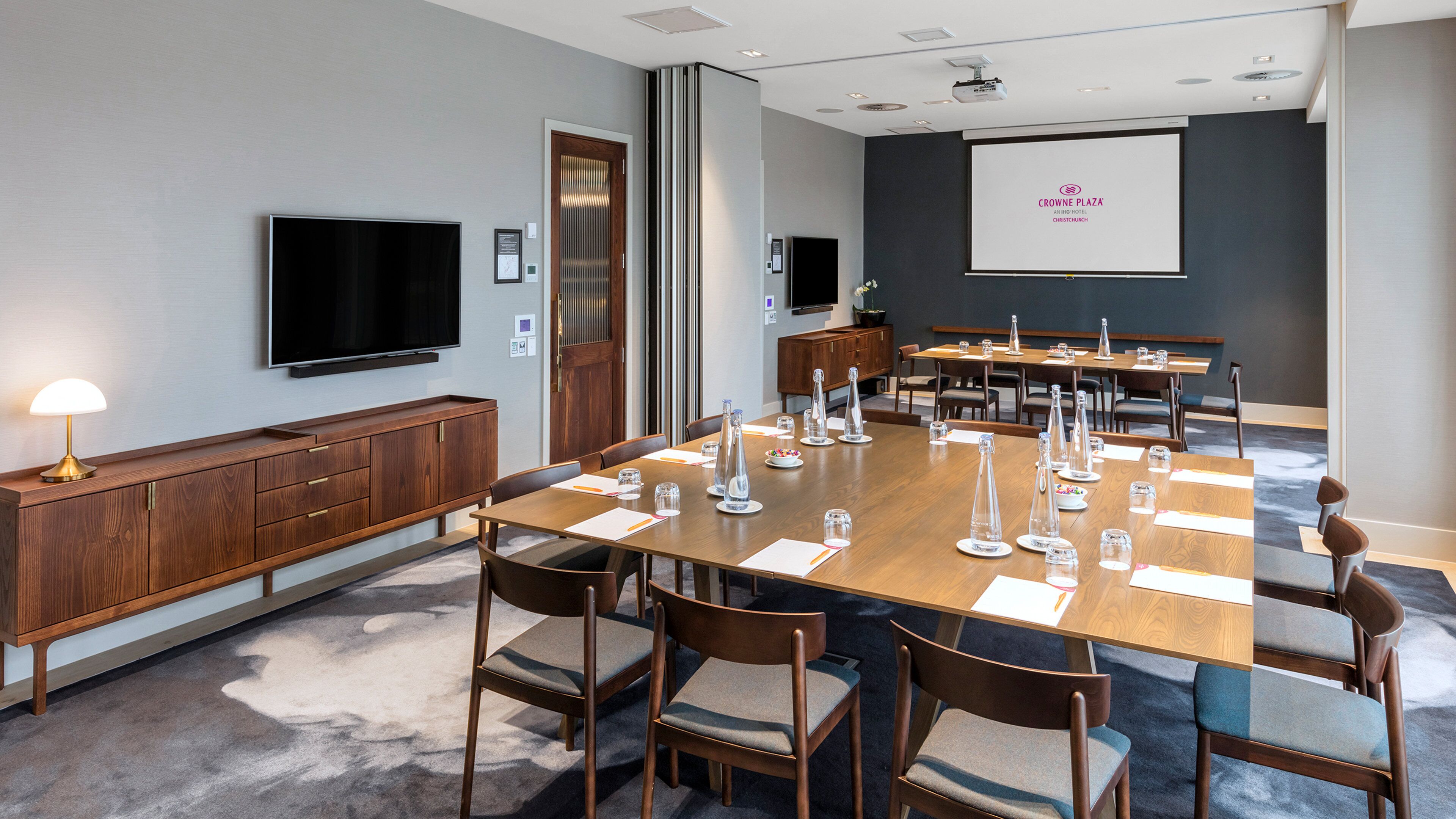 A conference room with a long table, chairs, a projector screen, and a television.
