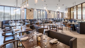 A modern restaurant with multiple dining areas, each equipped with tables, chairs, and ambient lighting.