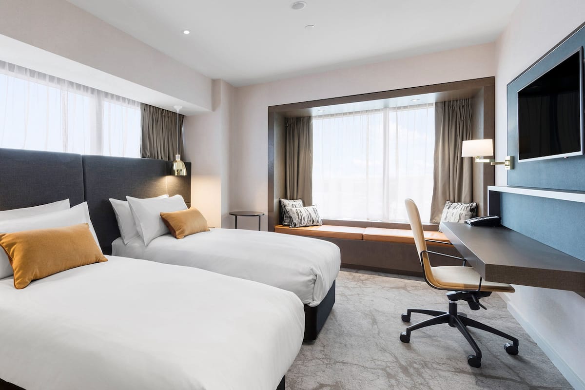 A hotel room with two beds, a desk, a chair, and a TV.