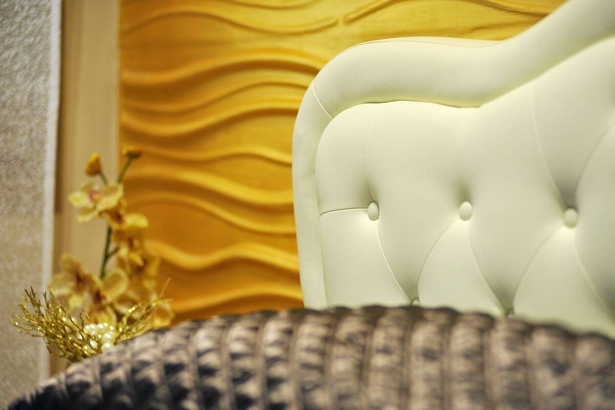 Un fauteuil blanc à dossier capitonné, agrémenté de motifs en relief, placé devant un mur jaune texturé.