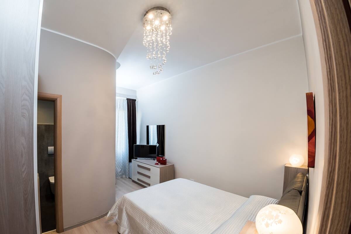 Une chambre moderne avec un grand lit, une télévision, une lampe de chevet et un lustre.