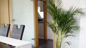 A modern interior with a dining area featuring a white table and black chairs, a potted plant, and a view into a kitchen area. - La Domus Premium (Lotte)