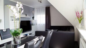A modern living room with a flat-screen TV, a dining table with chairs, a black sofa, and a white vase with flowers. - La Domus Premium (Lotte)