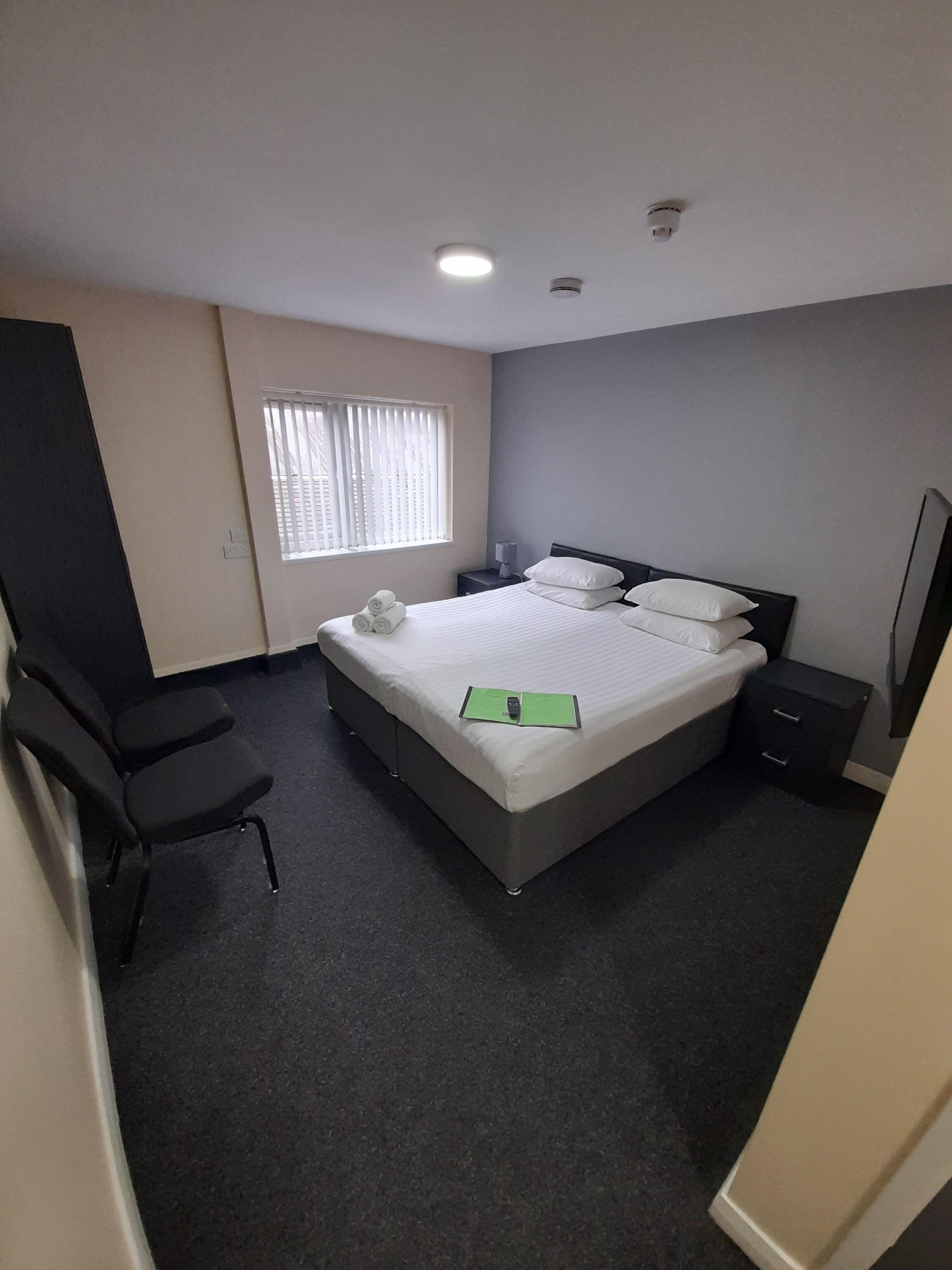 A hotel room with a bed, a desk, a chair, and a window with blinds.