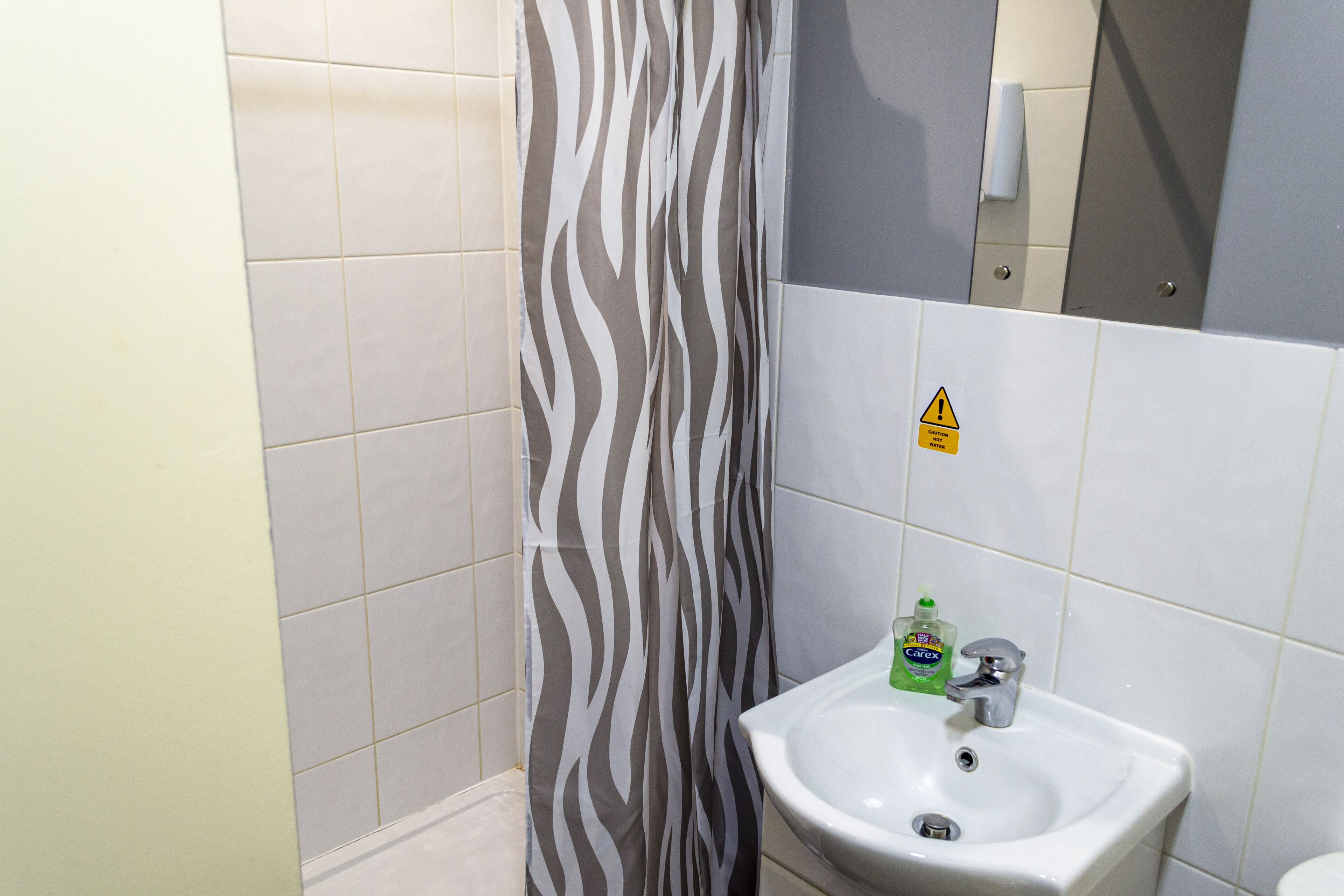 Un baño con cortina de ducha a rayas de cebra, un lavabo con dispensador de jabón y un letrero de precaución en la pared.
