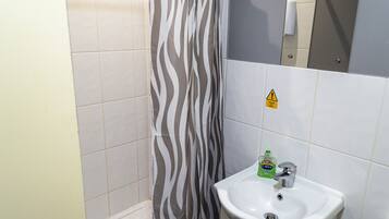 Un baño con cortina de ducha a rayas de cebra, un lavabo con dispensador de jabón y un letrero de precaución en la pared.
