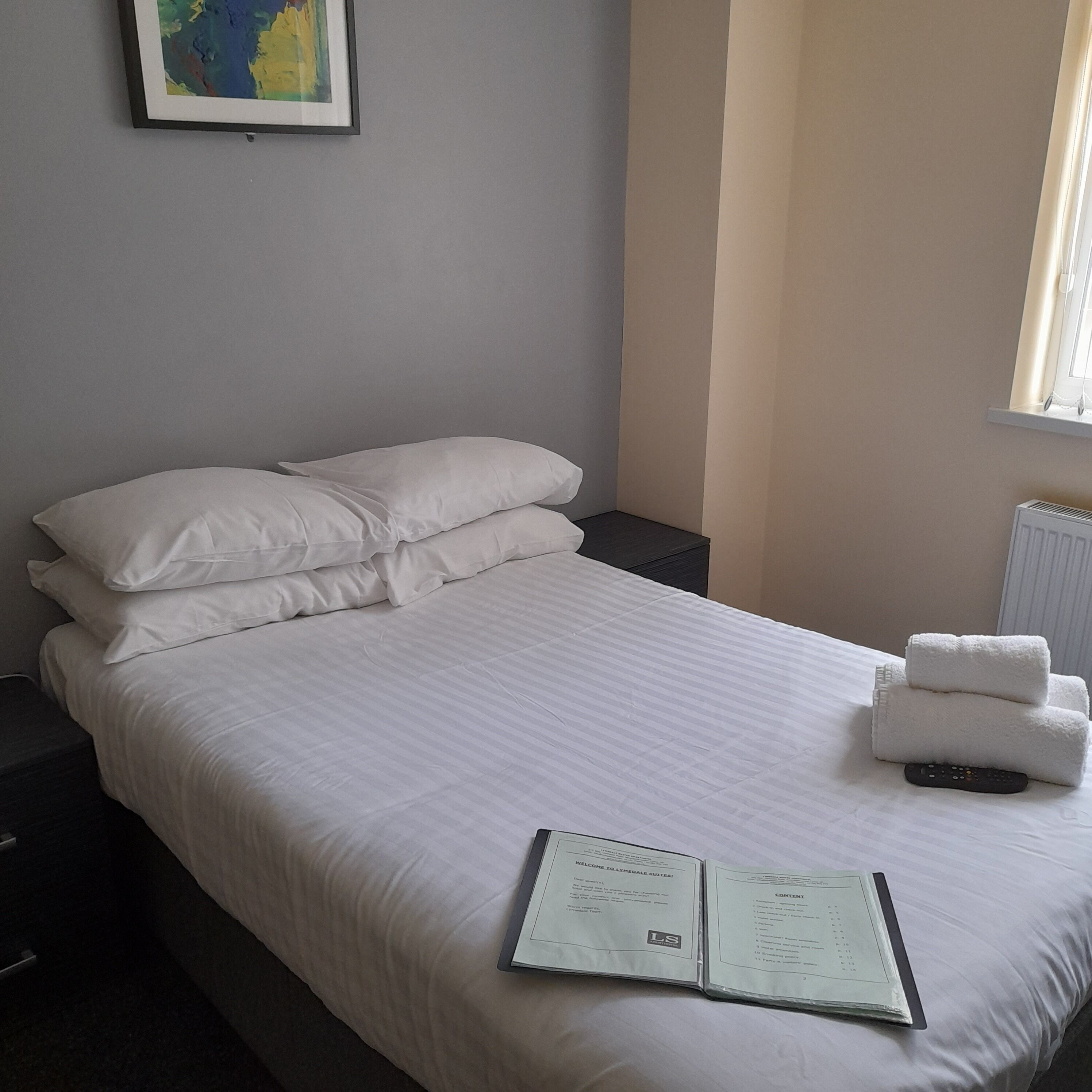Una cama bien hecha con sábanas blancas, un control remoto y una guía de bienvenida sobre la cama.