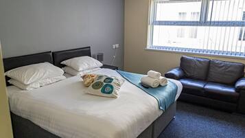 Une chambre d’hôtel avec un grand lit, un canapé en cuir marron et une fenêtre avec des stores.