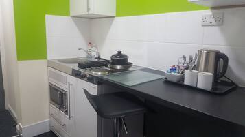 A compact kitchenette with a stove, sink, and a small oven. There are bar stools and a kettle on the counter.