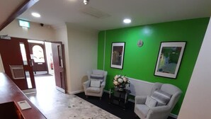 Un hall d’entrée doté d’un sol en terrazzo, de deux fauteuils, d’une petite table sur laquelle est posé un vase, et d’un mur d’accent de couleur verte.