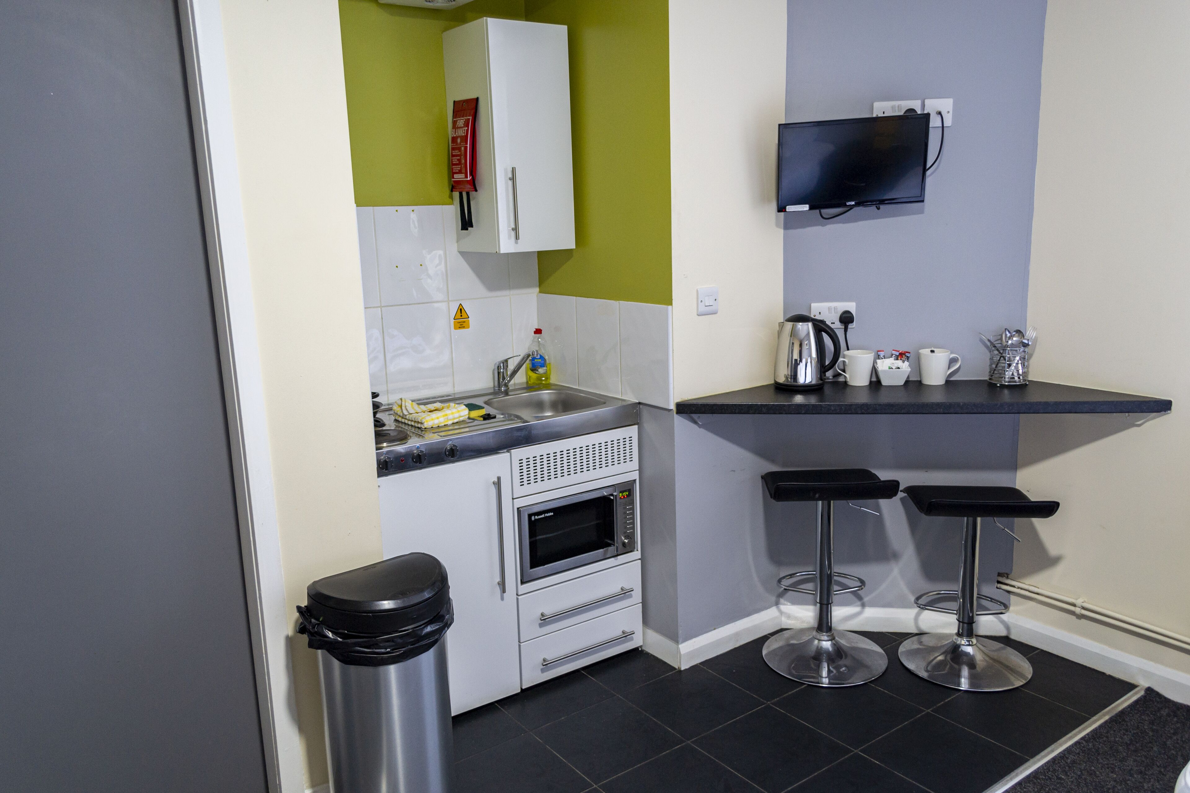 A compact kitchen with a microwave, sink, and two bar stools.